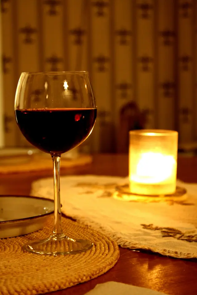 Copa de vino tinto junto a una vela encendida